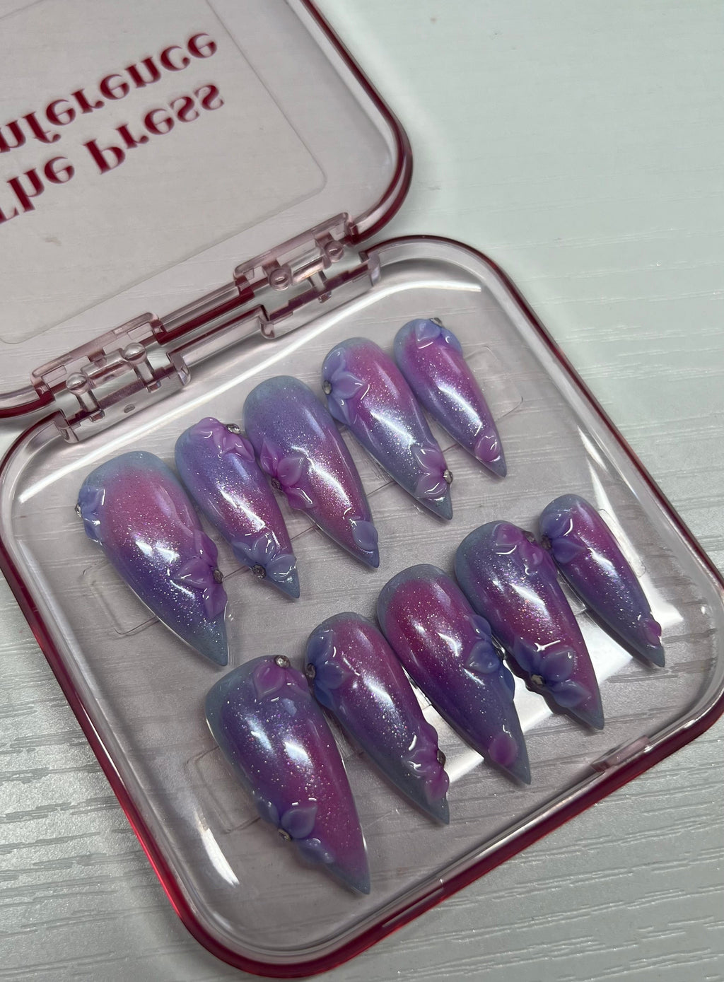 Set of purple and pink gradient false nails in a clear case with 'BBLG' branding.